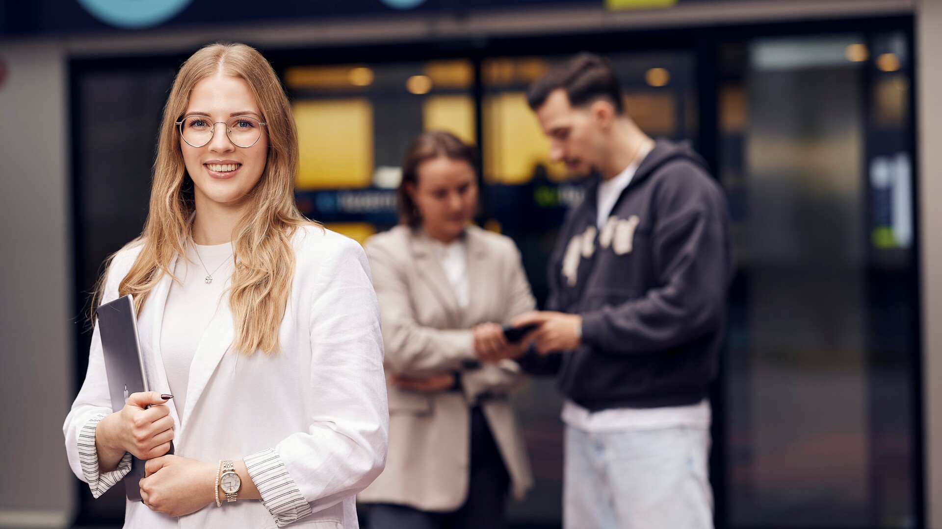 Studierende an der KV Luzern Berufsakademie Eine Studierende mit hellem Blazer steht vor dem Gebäude der KV Luzern Berufsakademie.